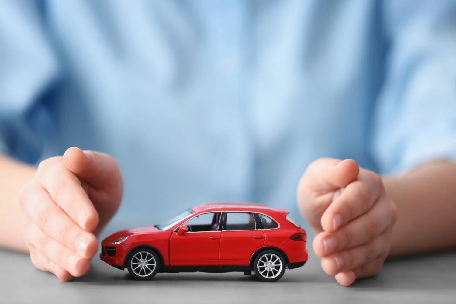 Hands cupped around a car during a yearly policy check